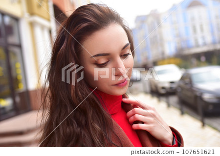 Portrait of a beautiful dreaming lady in a brown autumn coat on the street. 107651621