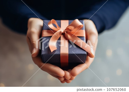 Beautiful gift and golden orange bow in female hands. Black Friday. Xmas or New Year present.  107652068
