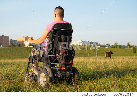 A young man in a wheelchair enjoying a sunset in the park, captured from behind A young man in a wheelchair enjoying a sunset in the park, captured from behind 107652814