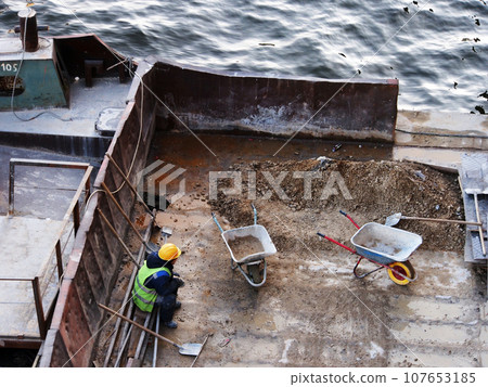 Construction work, a worker sits and rests on a barge, next to construction tools. Restoration work, construction and reconstruction, industrial production. 107653185