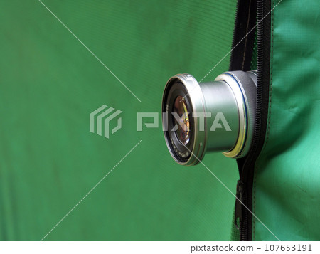 The camera lens looks out from a green tent, the photographer hides in the forest to take a photo of the wildlife for education. The camera lens looks out from a green tent, the photographer hides in the forest to take a photo of the wildlife for education. 107653191