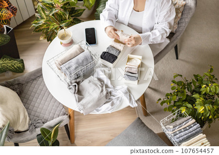 Unrecognizable woman sorting neatly folded linen cotton textile at container and basket on table 107654457