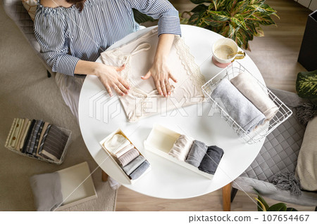 Smiling plus size woman folding linen nightdress in PVC container metal basket storage organizing Smiling plus size woman folding linen nightdress in PVC container metal basket storage organizing 107654467