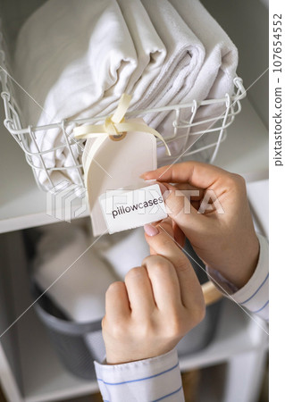 Woman hands organizing cotton pillowcase storage in basket with sticker tag mark at closet shelf 107654552
