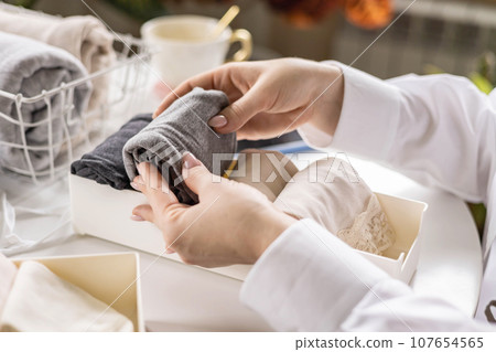 Housewife woman hands folded cotton linen domestic textile in box container and basket on table desk Housewife woman hands folded cotton linen domestic textile in box container and basket on table desk 107654565