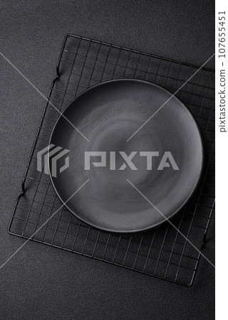 Empty ceramic round plate on dark textured concrete background Empty ceramic round plate on dark textured concrete background 107655451