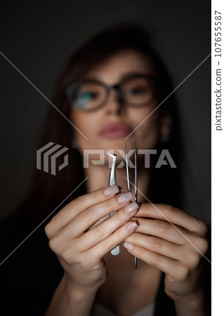 beautiful woman holding eyelashes tweezers on black background beautiful woman holding eyelashes tweezers on black background 107655587