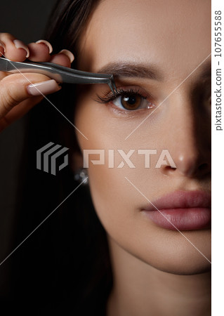 beautiful woman holding eyelashes tweezers on black background beautiful woman holding eyelashes tweezers on black background 107655588