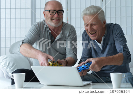 Two old men sitting at table and playing video game 107656364