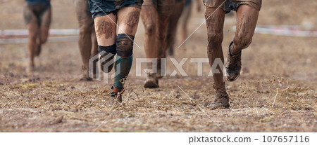 Group of participants in an obstacle course race running. They run very muddy. Concept of hardness and effort Group of participants in an obstacle course race running. They run very muddy. Concept of hardness and effort 107657116