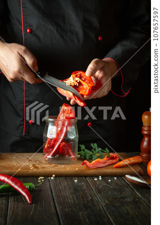 Peeling capsicums before slicing for canning in a jar. Chef's hands with a knife and a slice of bell pepper in a restaurant kitchen. Peeling capsicums before slicing for canning in a jar. Chef's hands with a knife and a slice of bell pepper in a restaurant kitchen. 107657597