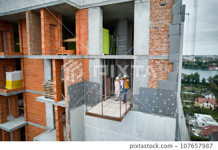 Man with wife and child standing inside residential building under construction. Urban district with newly constructed apartment building and family new residents real estate buyers. Drone view Man with wife and child standing inside residential building under construction. Urban district with newly constructed apartment building and family new residents real estate buyers. Drone view 107657987