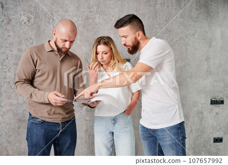 Man and woman looking at catalogue while choosing interior design for new apartment with professional designer. Couple planning home renovation and redesigning with specialist. 107657992