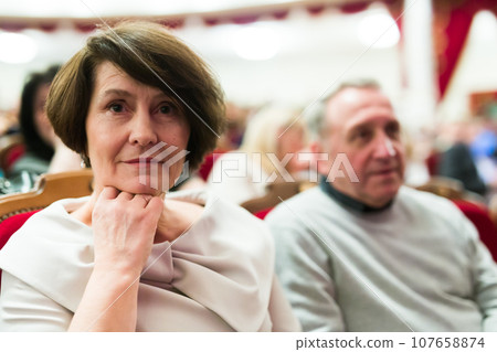 Mature man and woman in theater watching a performance Mature man and woman in theater watching a performance 107658874