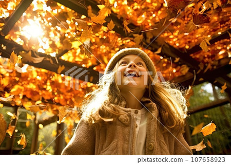 a little girl playing with autumn leaves in the park, she is laughing and looking up to the sky stock photo a little girl playing with autumn leaves in the park, she is laughing and looking up to the sky stock photo 107658923
