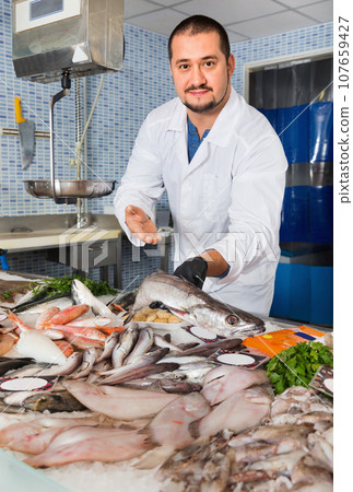 Man in glove behind counter shows fish in his hand 107659427