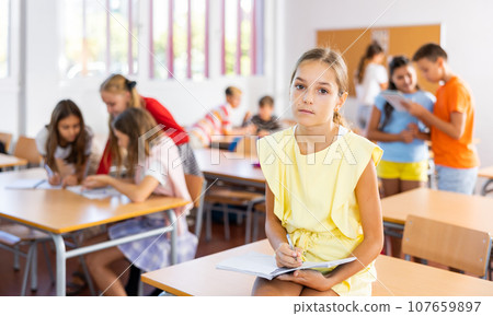 Upset tween girl sitting on table in schoolroom during recess 107659897