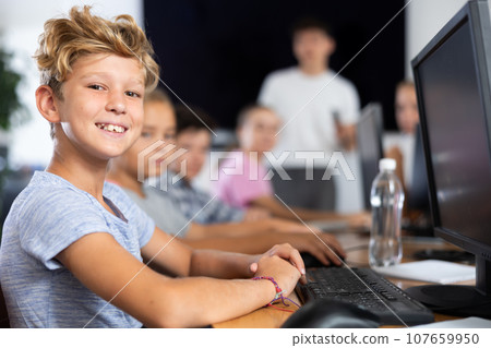 Smiling preteen boy sitting at computer table in training room Smiling preteen boy sitting at computer table in training room 107659950