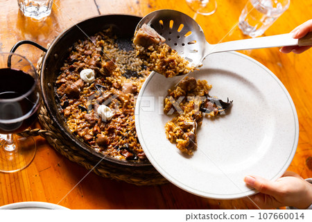 Customer putting paella from pan to plate Customer putting paella from pan to plate 107660014