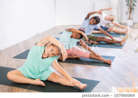 Active children exercising during yoga class in fitness center - vakrasana pose Active children exercising during yoga class in fitness center - vakrasana pose 107660069
