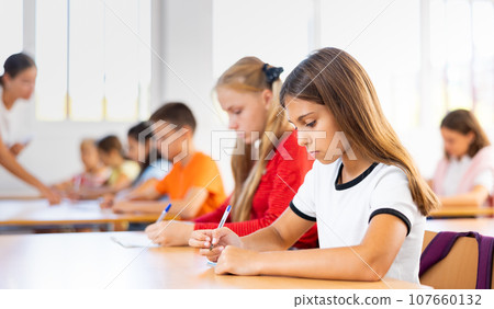 Interested diligent preteen schoolgirl writing exercises at lessons Interested diligent preteen schoolgirl writing exercises at lessons 107660132
