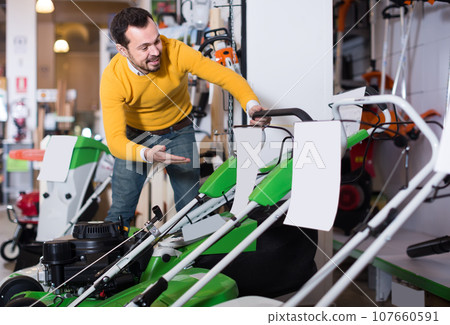 concentrated guy deciding on best lawnmower in garden equipment shop 107660591