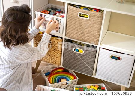 Woman mother applying paper sticker with name title on basket container clean out of childish toys 107660936