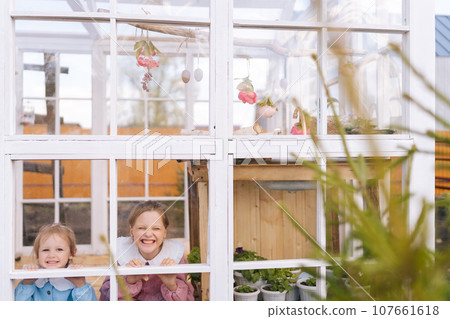 Portrait of joyful pretty little children girls sisters in beautiful dress standing posing in summer gazebo house on sunny day smiling looking at camera with happy expression, through window. Portrait of joyful pretty little children girls sisters in beautiful dress standing posing in summer gazebo house on sunny day smiling looking at camera with happy expression, through window. 107661618