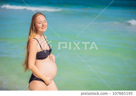 Radiant pregnant woman in a swimsuit, amid the stunning backdrop of a turquoise sea. Serene beauty of maternity by the shore 107665195