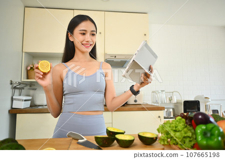 Beautiful young woman preparing ingredients for making healthy salad and following online recipe on digital tablet Beautiful young woman preparing ingredients for making healthy salad and following online recipe on digital tablet 107665198