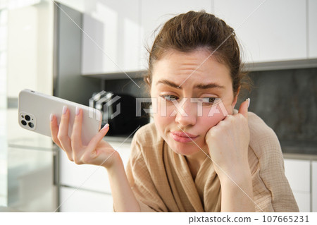 Attractive young cheerful girl baking at the kitchen, making dough, holding recipe book, having ideas Attractive young cheerful girl baking at the kitchen, making dough, holding recipe book, having ideas 107665231