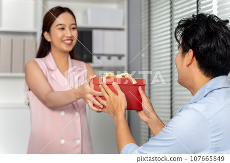 Asian business woman giving a gift box to a coworker in the office setting environment. Thank you and success celebration in the corporate business office concept. 107665849