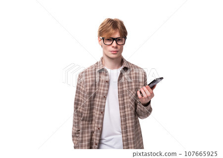 caucasian young man with red hair in a shirt actively uses a smartphone caucasian young man with red hair in a shirt actively uses a smartphone 107665925