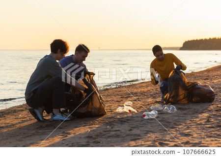 Earth day. Volunteers activists collects garbage cleaning of beach coastal zone. Woman and mans puts plastic trash in garbage bag on ocean shore. Environmental conservation coastal zone cleaning 107666625