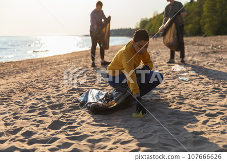 Earth day. Volunteers activists collects garbage cleaning of beach coastal zone. Woman and mans puts plastic trash in garbage bag on ocean shore. Environmental conservation coastal zone cleaning 107666626