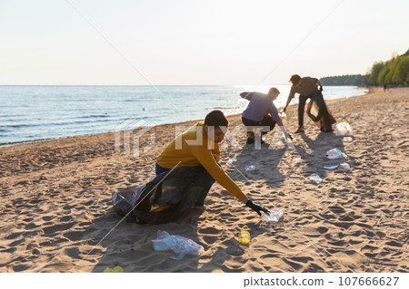 Earth day. Volunteers activists collects garbage cleaning of beach coastal zone. Woman and mans puts plastic trash in garbage bag on ocean shore. Environmental conservation coastal zone cleaning 107666627
