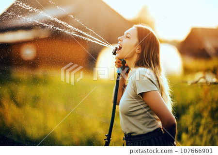 Garden hose for watering vegetables in hands of young woman who performed comic pantomime with splashes. 107666901