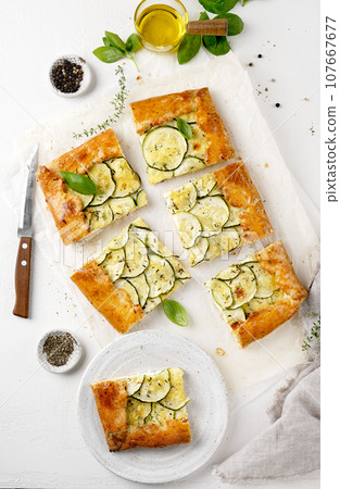 Healthy baked zucchini galette tart cutted into pieces on light table, top view Healthy baked zucchini galette tart cutted into pieces on light table, top view 107667677