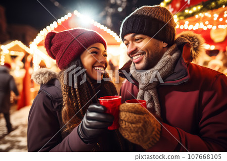 Happy multiracial couple drinking mulled wine at Christmas fair in festively decorated city Happy multiracial couple drinking mulled wine at Christmas fair in festively decorated city 107668105
