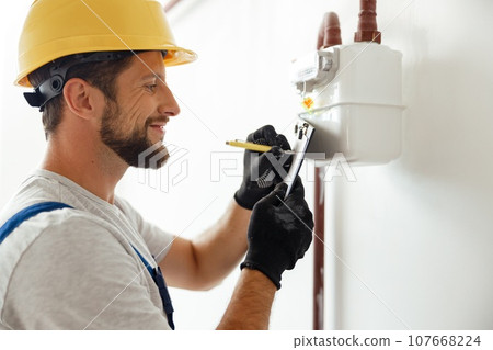 Happy professional heating fitter making notes while checking gas consumption at gas pipe and meter counter Happy professional heating fitter making notes while checking gas consumption at gas pipe and meter counter 107668224