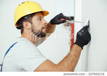 Portrait of male worker professional electrician in uniform installing electrical outlet in apartment after renovation work 107668236