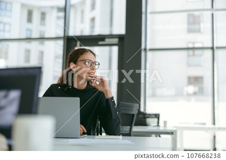 Smiling stylish businesswoman working on laptop sitting in modern office background Smiling stylish businesswoman working on laptop sitting in modern office background 107668238