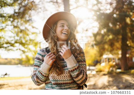 Stylish woman enjoying autumn weather in the sunny park. Enjoying nature. Fashion, style concept. 107668331