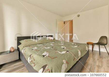 a bed in a room with white walls and wood flooring on the wall, there is a chair next to the bed 107668552