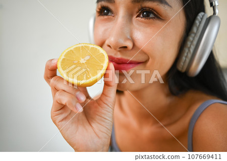 Close up beauty woman in headphone holding half lemon. Dieting and healthy lifestyle concept Close up beauty woman in headphone holding half lemon. Dieting and healthy lifestyle concept 107669411