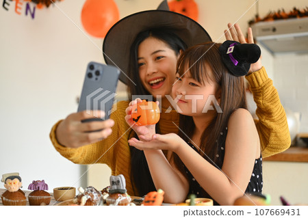 Happy young mother and her daughter taking a selfie on smart phone in Halloween decorated kitchen 107669431