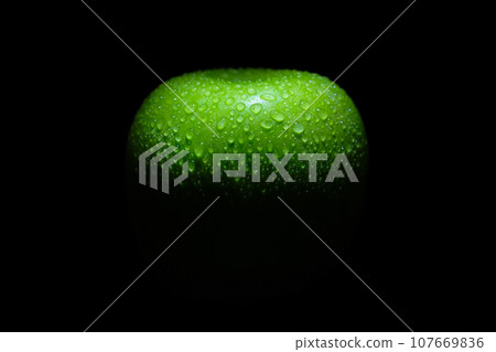 Green ripe apple with water drops on a black background, close up. Conceptual background Green ripe apple with water drops on a black background, close up. Conceptual background 107669836