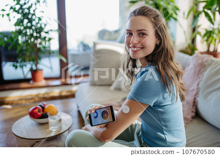 Woman with diabetes using continuous glucose monitor. Diabetic woman connecting CGM to smartphone to monitor her blood sugar levels in real time. Woman with diabetes using continuous glucose monitor. Diabetic woman connecting CGM to smartphone to monitor her blood sugar levels in real time. 107670580