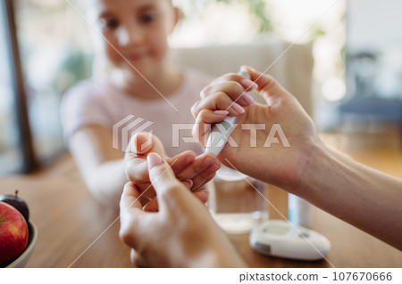 Close up of mother checking girl's blood glucose level using fingerstick glucose meter. Endocrinologist waiting for results from blood test. 107670666