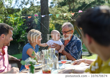 Cute baby playing with grandfather at summer garden party. The grandfather holding baby boy in his arms and smiling. 107670674